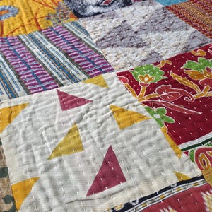 Puede incluir: Primer plano de un edred&oacute;n de retazos con una variedad de cuadrados de tela coloridos. El edred&oacute;n presenta patrones geom&eacute;tricos, dise&ntilde;os florales y estampados abstractos en tonos de rojo, amarillo, azul y morado. La costura es visible.