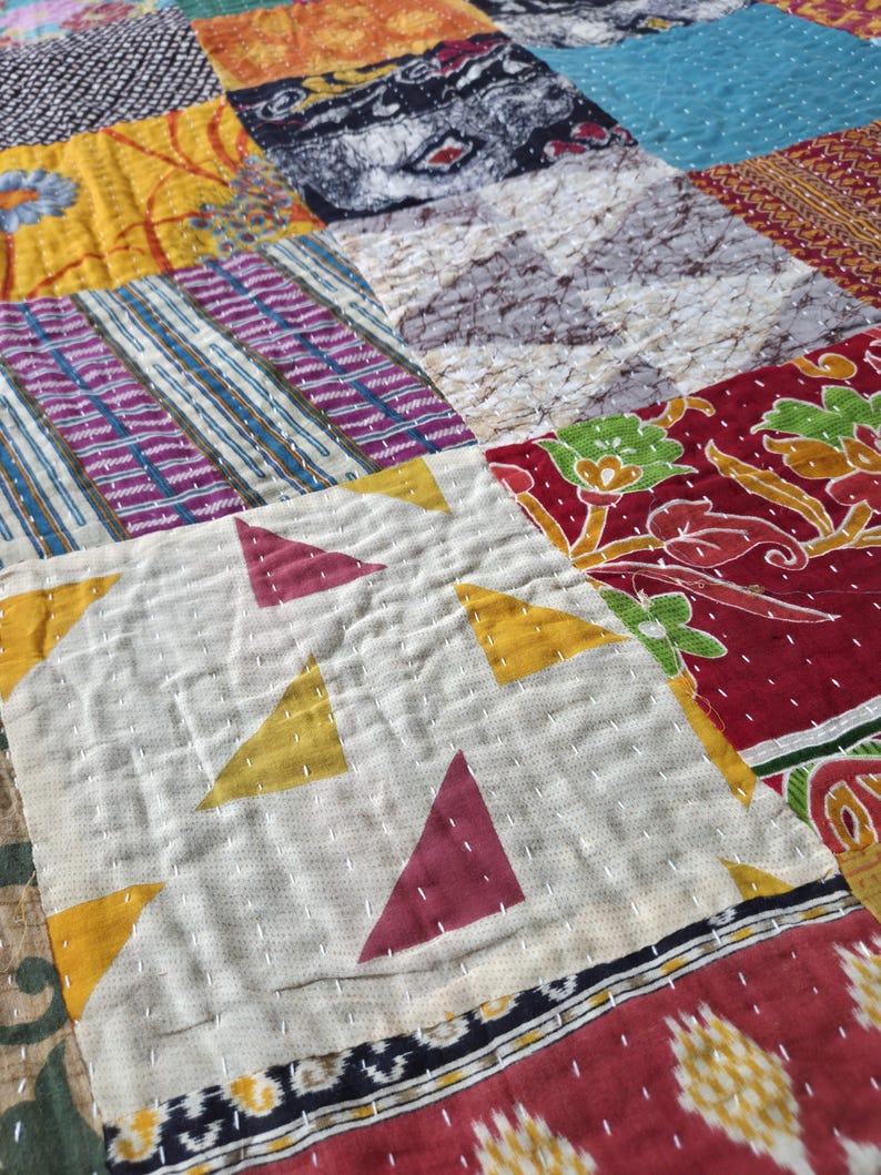 Puede incluir: Primer plano de un edred&oacute;n de retazos con una variedad de cuadrados de tela coloridos. El edred&oacute;n presenta patrones geom&eacute;tricos, dise&ntilde;os florales y estampados abstractos en tonos de rojo, amarillo, azul y morado. La costura es visible.