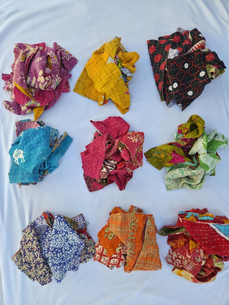 May include: Nine colorful, patterned fabric scraps in various colors, including purple, yellow, red, black, blue, pink, orange, and green. The fabrics appear to be quilted or stitched with decorative patterns. The scraps are arranged on a white surface.