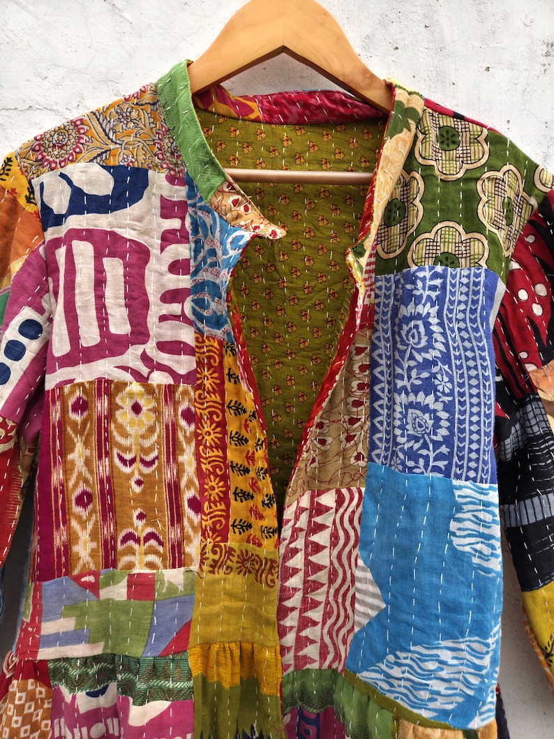 May include: A patchwork jacket with a variety of colorful fabric patterns. The jacket is hanging on a wooden hanger. The design includes floral, geometric, and abstract shapes in shades of red, blue, green, and yellow.