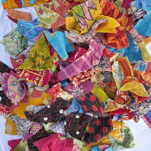 May include: A collection of colorful fabric scraps with intricate stitching. The pieces feature a variety of patterns, including floral and geometric designs, in shades of red, blue, yellow, and pink. The fabric appears to be repurposed or vintage.