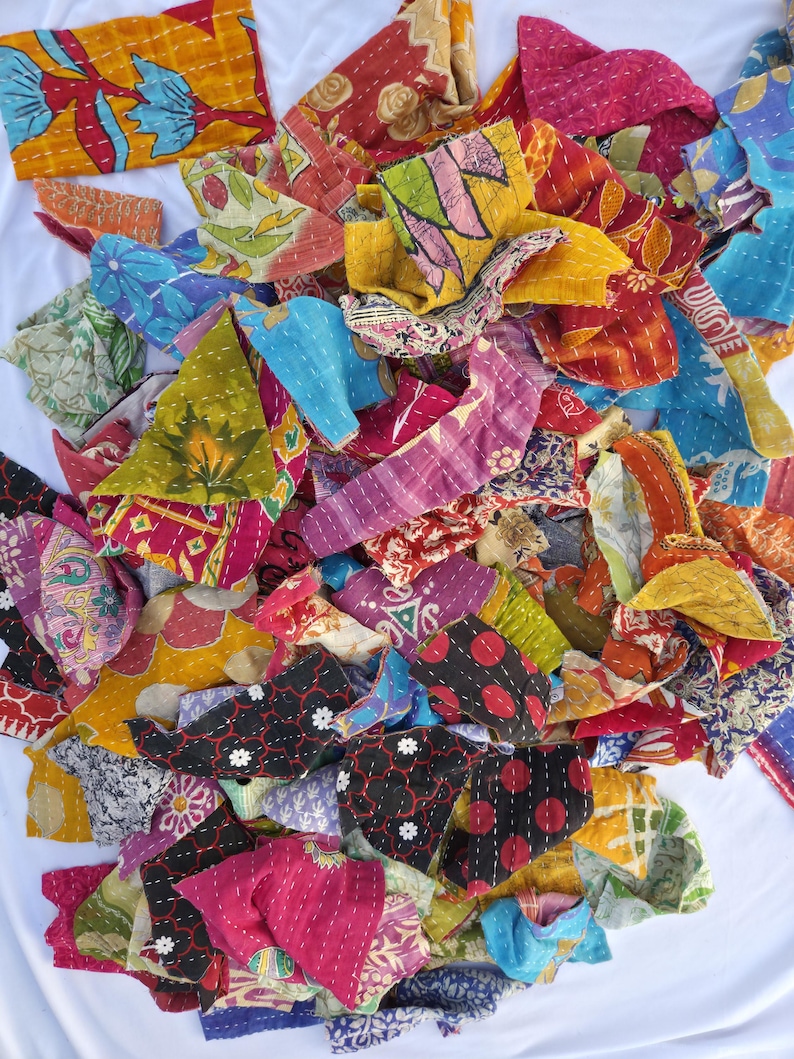 May include: A collection of colorful fabric scraps with intricate stitching. The pieces feature a variety of patterns, including floral and geometric designs, in shades of red, blue, yellow, and pink. The fabric appears to be repurposed or vintage.