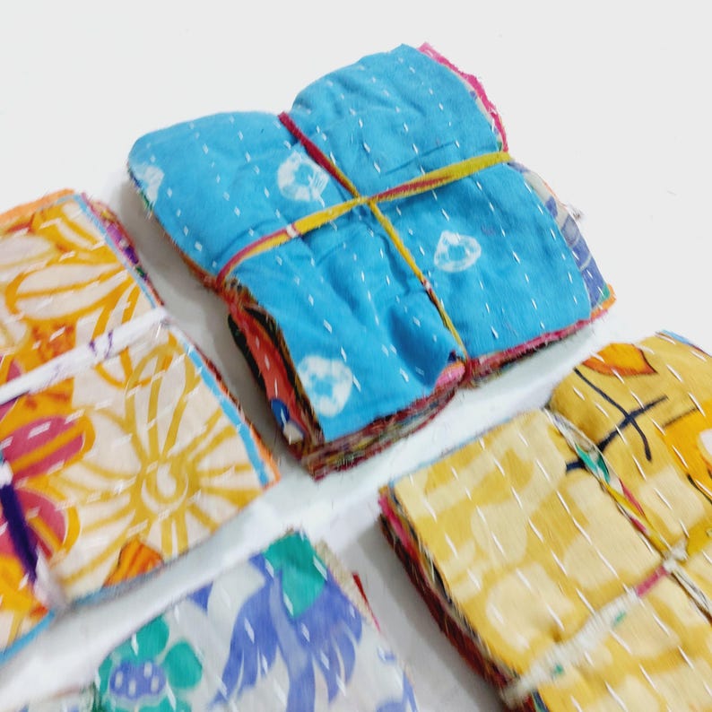May include: A collection of colorful, patterned fabric squares, bundled and tied with elastic bands. The fabrics feature various designs, including floral and abstract patterns, in shades of blue, yellow, and orange. White stitching is visible.