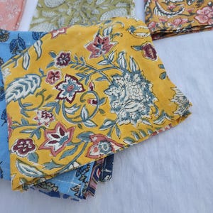 May include: Folded fabric napkins with floral patterns. The napkins feature a variety of colors, including yellow, blue, and pink. The floral designs include leaves and flowers. The napkins are made of a soft material.