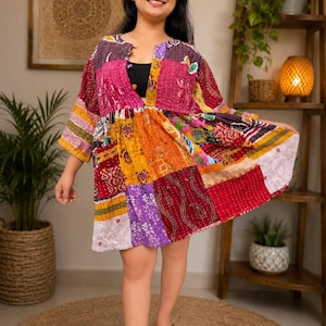 Könnte beinhalten: Ein Patchwork-Kleid in leuchtenden Farben, darunter Rosa, Orange und Lila. Das Kleid hat ein einzigartiges Design mit verschiedenen Stoffmustern und -strukturen. Das Kleid ist knielang und hat kurze Ärmel.