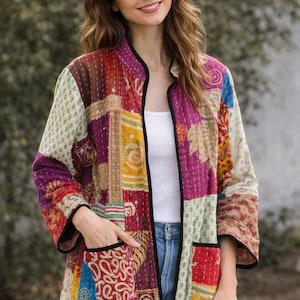 May include: A quilted jacket featuring a patchwork design with various floral and geometric patterns in shades of red, yellow, blue, and cream. The jacket has a mandarin collar, three-quarter length sleeves, two front pockets, and black trim.