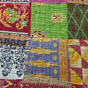 Puede incluir: Primer plano de un textil patchwork con una variedad de colores y patrones. El edred&oacute;n presenta cuadrados de tela roja, verde, morada y amarilla, cada uno con dise&ntilde;os &uacute;nicos y detalles cosidos. La est&eacute;tica general es vibrante y artesanal.
