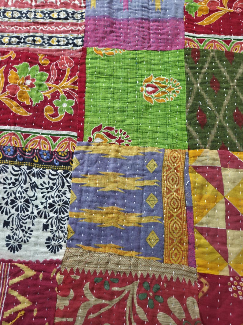 Puede incluir: Primer plano de un textil patchwork con una variedad de colores y patrones. El edred&oacute;n presenta cuadrados de tela roja, verde, morada y amarilla, cada uno con dise&ntilde;os &uacute;nicos y detalles cosidos. La est&eacute;tica general es vibrante y artesanal.