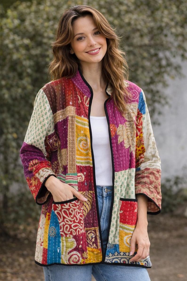 May include: A quilted jacket featuring a patchwork design with various floral and geometric patterns in shades of red, yellow, blue, and cream. The jacket has a mandarin collar, three-quarter length sleeves, two front pockets, and black trim.