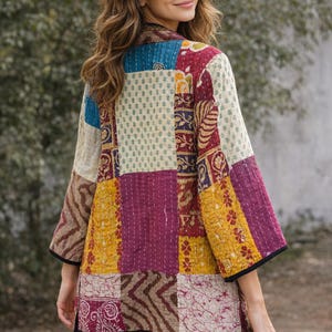 May include: A quilted jacket featuring a patchwork design of various floral and geometric patterns in shades of maroon, mustard yellow, cream, and blue. The garment has three-quarter length sleeves, a straight hem, and black trim along the edges.