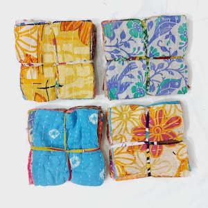 May include: Four bundles of colorful fabric squares, each tied with a contrasting ribbon. The fabrics feature floral and abstract patterns in shades of yellow, blue, orange, and pink. The squares are stitched together with white thread.