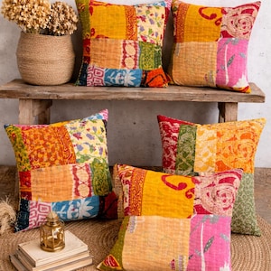 Könnte beinhalten: Eine Sammlung bunter Patchwork-Zierkissen in Gelb-, Orange-, Rot- und Blautönen. Die Kissen sind auf einer Holzbank und einem gewebten Teppich angeordnet und schaffen eine gemütliche Atmosphäre.