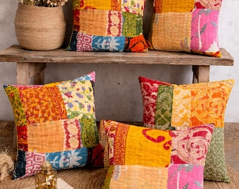 May include: A collection of colorful patchwork throw pillows in various sizes. The pillows feature a mix of vibrant fabrics in yellow, orange, red, blue, and pink. They are arranged on a wooden bench and a woven jute rug, creating a cozy, bohemian aesthetic.
