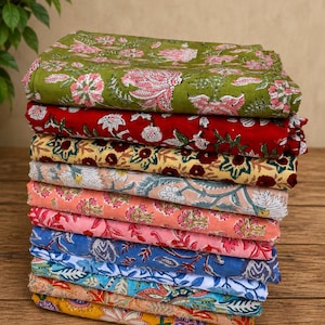 May include: A vertical stack of ten folded fabric pieces, each featuring a distinct floral block print pattern. The textiles display a variety of colors including olive green, deep red, mustard yellow, soft pink, light blue, and white.