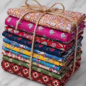 May include: A stack of colorful fabric squares tied with twine. The fabrics feature floral patterns in shades of pink, yellow, blue, and red. The stack is bound with natural twine, creating a rustic and charming presentation.