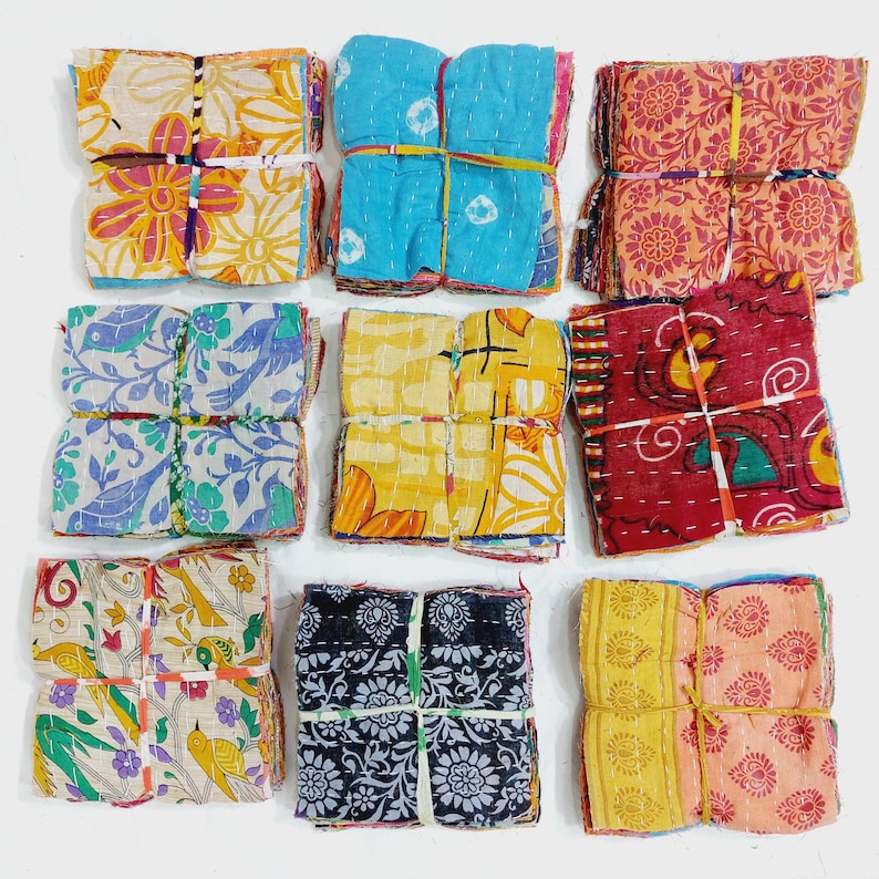 May include: Nine bundles of colorful fabric squares, each tied with a rubber band. The fabrics feature floral and geometric patterns in various colors, including blue, yellow, red, and orange. The squares appear to be made of a lightweight material.