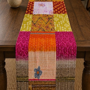 Könnte beinhalten: Ein farbenfroher Patchwork-Tischläufer mit verschiedenen Mustern und Farben, darunter Rosa, Orange, Gelb und Braun. Der Läufer hat ein Blumenmuster und liegt auf einem Holztisch. Der Läufer ist etwa 152 cm lang.