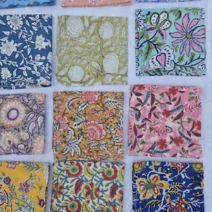 May include: An assortment of colorful, square fabric swatches with floral patterns. The swatches feature various designs in shades of blue, pink, yellow, green, and purple. The patterns include detailed flower and leaf motifs.