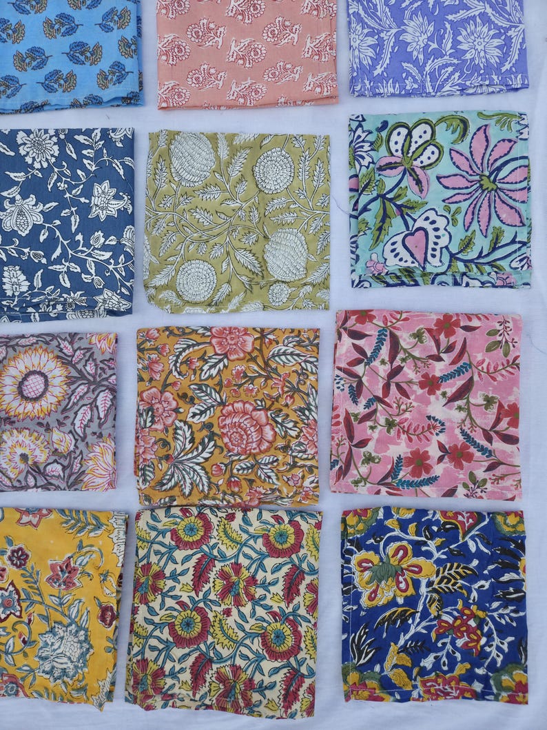 May include: An assortment of colorful, square fabric swatches with floral patterns. The swatches feature various designs in shades of blue, pink, yellow, green, and purple. The patterns include detailed flower and leaf motifs.