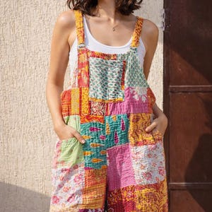 Pode incluir: Macacão patchwork multicolorido com alças ajustáveis e bolsos. A peça apresenta um design patchwork com tons de rosa, amarelo, verde e vermelho. O macacão é feito de um design patchwork.