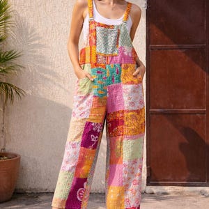 Könnte beinhalten: Ein Patchwork-Jumpsuit in leuchtenden Farben, darunter Rosa, Gelb und Grün, mit einem weißen Tanktop darunter. Der Jumpsuit hat weite Beine und verstellbare Träger. Das Model trägt weiße Sandalen.