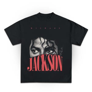 May include: Black t-shirt featuring a grayscale image of Michael Jackson's eyes and part of his face. The name "JACKSON" is printed in large red letters below the eyes, with "MICHAEL" above.