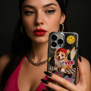 May include: A silver iPhone case featuring a cartoon corgi wearing a red hat and mustache, with the text "YES!" and a smiley face. The case is held up in front of a person.