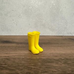 May include: A pair of vibrant yellow wellington boots. The boots are made of a smooth material and have a classic design. They are standing upright on a wooden surface, with a neutral grey background.