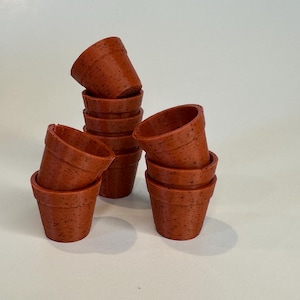 以下が含まれることがあります： テラコッタ色の小さな植木鉢のコレクション。鉢は積み重ねられ、魅力的に配置されています。鉢は質感のある表面とクラシックなデザインで、小さな植物や多肉植物に適しています。