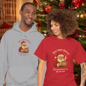 Könnte beinhalten: Ein hellgrauer Kapuzenpullover und ein rotes T-Shirt, beide mit einer Grafik vom Weihnachtsmann, der eine dampfende Tasse hält, sowie dem Text "Only drink coffee? You could be on the no-tea list!" in einer dekorativen Schriftart darüber und darunter.