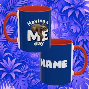 May include: A blue ceramic mug with a bright red interior and handle. One side features a brown sloth illustration with the text "Having a ME day". The other side displays the word "NAME" in large white letters against the blue background.