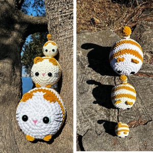 May include: Crocheted cat plush toys in white and orange. The toys are stacked on a tree and a rock. The cats have black eyes, pink noses, and yellow ears and paws. The toys are handmade and have a round shape.