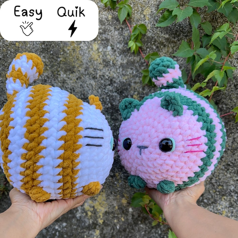 May include: Two handmade crochet cat plushies. One is white and gold striped, the other is pink and green striped. Both have black eyes and small noses. The image has the text "Easy Quik" in the top left corner.