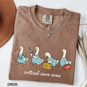A "Espresso" Comfort Colors t-shirt featuring four cartoon geese dressed as an ICU medical team, with the text "critical care crew" printed below.