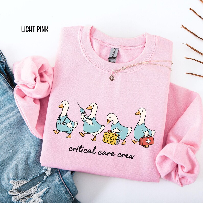 A "Light Pink" sweatshirt, featuring four cartoon geese dressed as an ICU medical team, with the text "critical care crew" printed below.