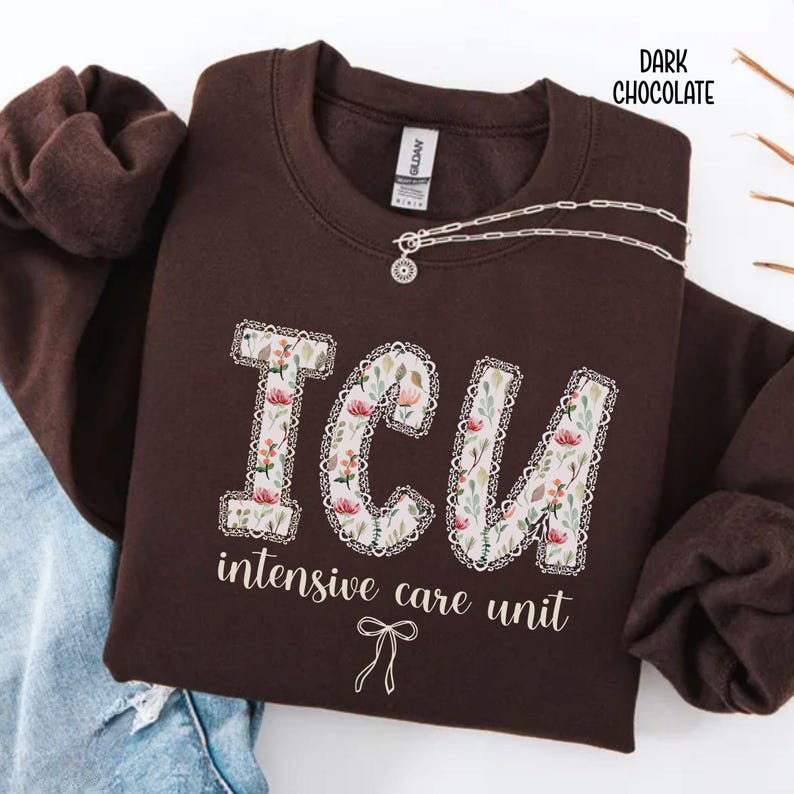 A "Dark Chocolate" sweatshirt, featuring the letters "ICU" in a block font filled with a green, pink, and white floral pattern with a decorative border, and the words "intensive care unit" and a bow below.