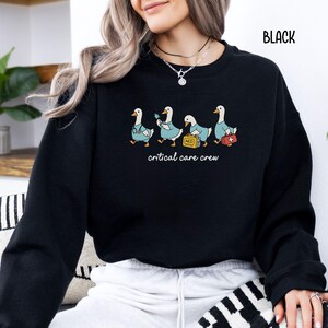 A "Black" sweatshirt, featuring four cartoon geese dressed as an ICU medical team, with the text "critical care crew" printed below.