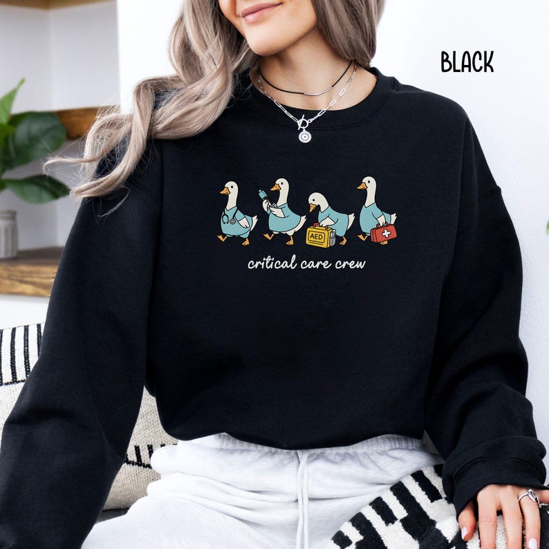 A "Black" sweatshirt, featuring four cartoon geese dressed as an ICU medical team, with the text "critical care crew" printed below.