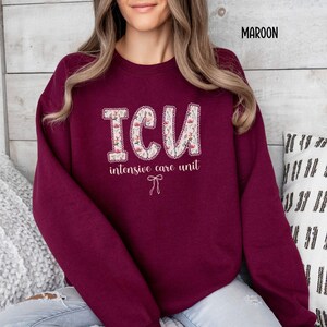 A "Maroon" sweatshirt, featuring the letters "ICU" in a block font filled with a green, pink, and white floral pattern with a decorative border, and the words "intensive care unit" and a bow below.