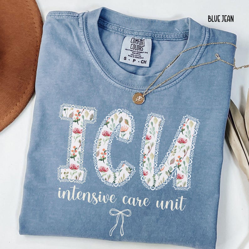 A "Blue Jean" Comfort Colors t-shirt, featuring the letters "ICU" in a block font filled with a green, pink, and white floral pattern with a decorative border, and the words "intensive care unit" and a bow below.