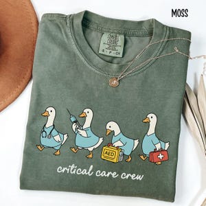 A "Moss" Comfort Colors t-shirt featuring four cartoon geese dressed as an ICU medical team, with the text "critical care crew" printed below.