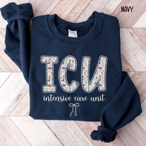 A "Navy" sweatshirt, featuring the letters "ICU" in a block font filled with a green, pink, and white floral pattern with a decorative border, and the words "intensive care unit" and a bow below.