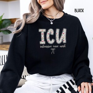 A "Black" sweatshirt, featuring the letters "ICU" in a block font filled with a green, pink, and white floral pattern with a decorative border, and the words "intensive care unit" and a bow below.