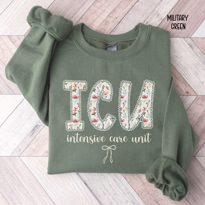 A "Military Green" sweatshirt, featuring the letters "ICU" in a block font filled with a green, pink, and white floral pattern with a decorative border, and the words "intensive care unit" and a bow below.