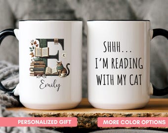 May include: White ceramic mug with a black handle and rim. One side features a letter "E" with books, a cat, and the name "Emily." The other side reads "Shhh... I'm reading with my cat."
