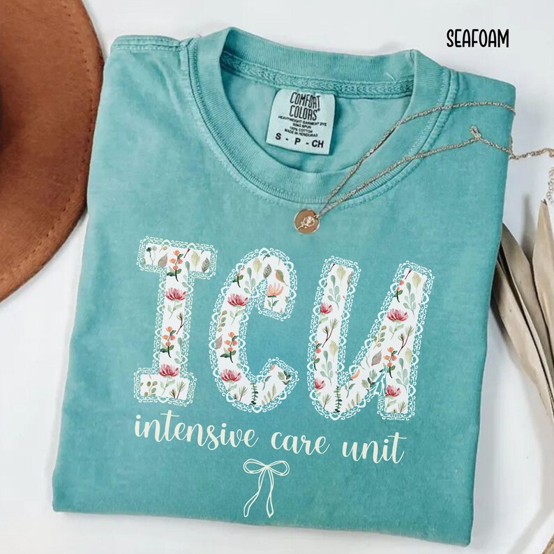A "Seafoam" Comfort Colors t-shirt, featuring the letters "ICU" in a block font filled with a green, pink, and white floral pattern with a decorative border, and the words "intensive care unit" and a bow below.