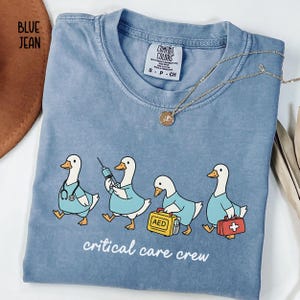 A "Blue Jean" Comfort Colors t-shirt featuring four cartoon geese dressed as an ICU medical team, with the text "critical care crew" printed below.