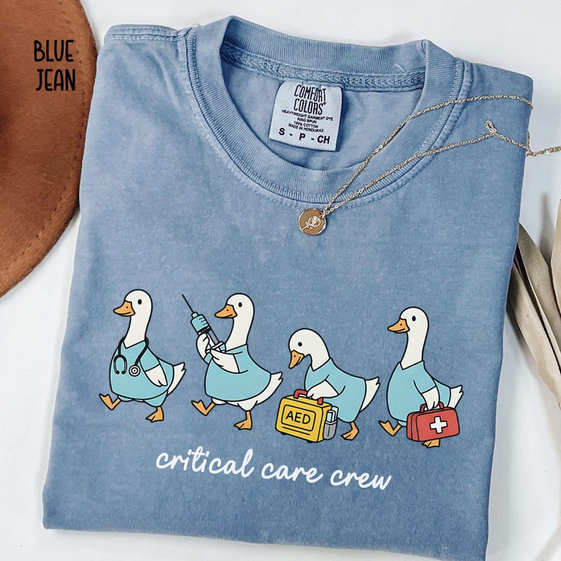 A "Blue Jean" Comfort Colors t-shirt featuring four cartoon geese dressed as an ICU medical team, with the text "critical care crew" printed below.