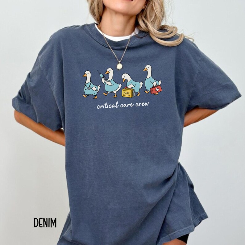 A "Denim" Comfort Colors t-shirt featuring four cartoon geese dressed as an ICU medical team, with the text "critical care crew" printed below.