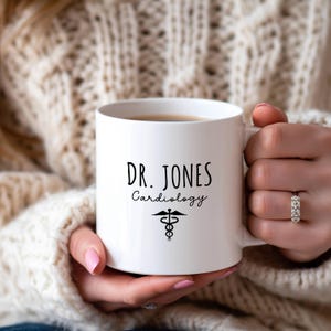 White ceramic mug features a custom personalized design with 'Dr. Jones Cardiology' and a medical symbol.